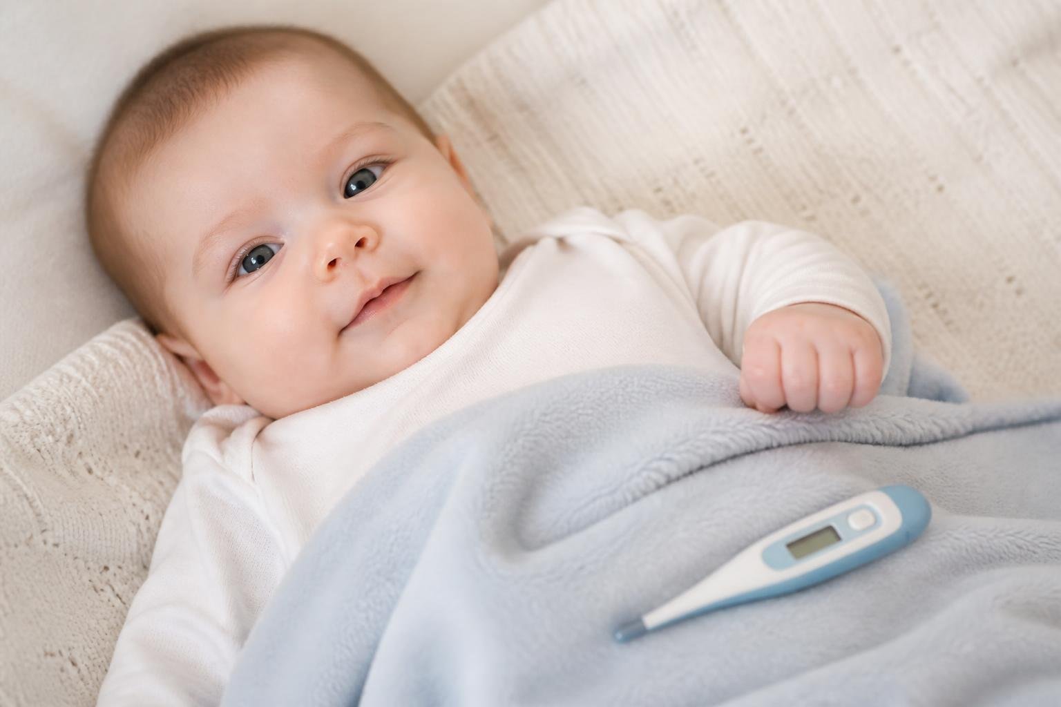 Digital baby thermometer beside a calm baby on a soft blanket