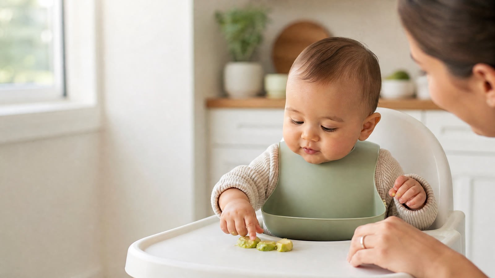 Baby exploring soft textured food while seated upright with a caregiver supervising