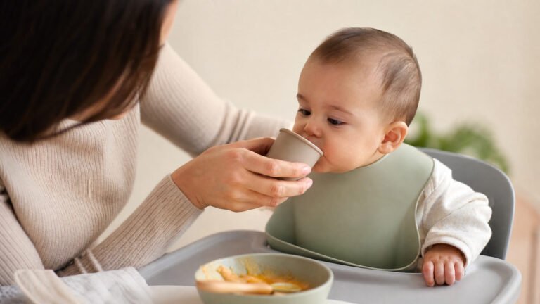 Baby water: infant practicing a small sip from an open cup around 6 months.